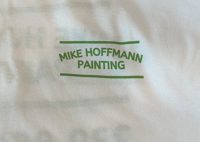 Stacks of white work tees with a 1-color green logo