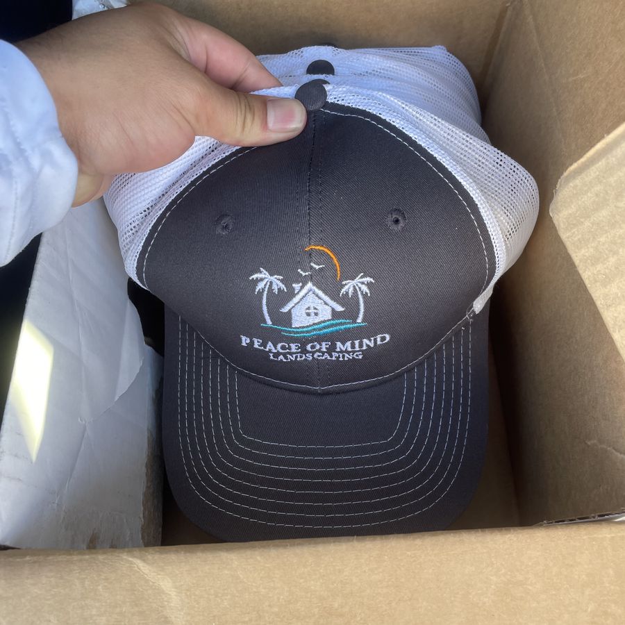 Grey trucker hat embroidered with the Peace of Mind Landscaping logo