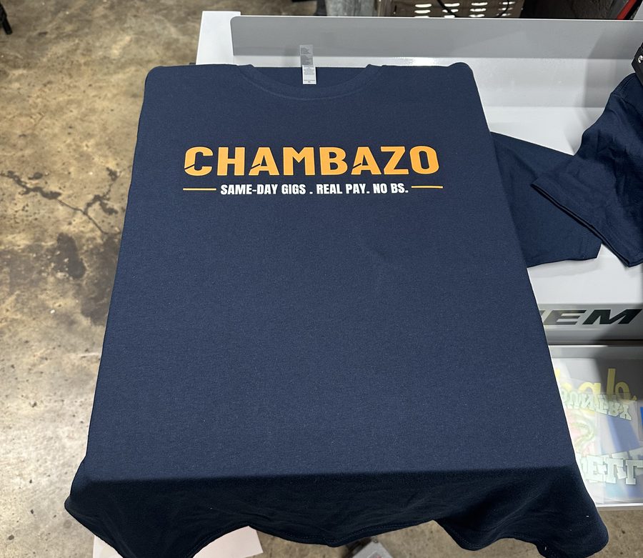 Navy tee with an orange logo print on the screen printing press